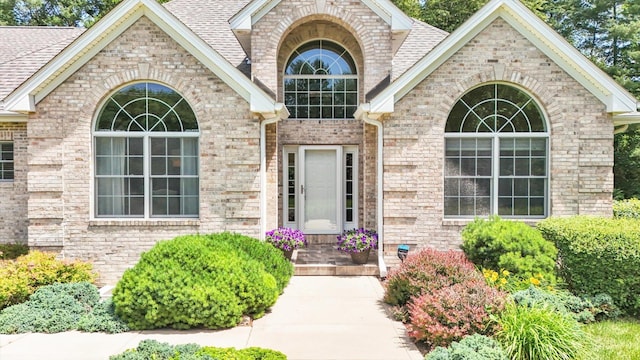 doorway to property with brick siding and a shingled roof