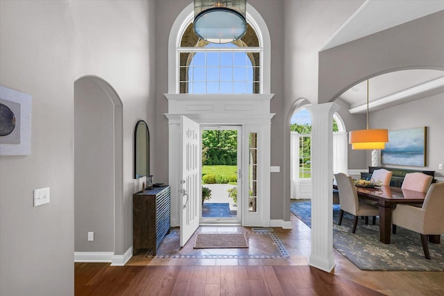 entryway featuring arched walkways, hardwood / wood-style floors, a towering ceiling, and baseboards