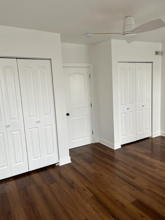 unfurnished bedroom with multiple closets, dark wood-type flooring, and ceiling fan