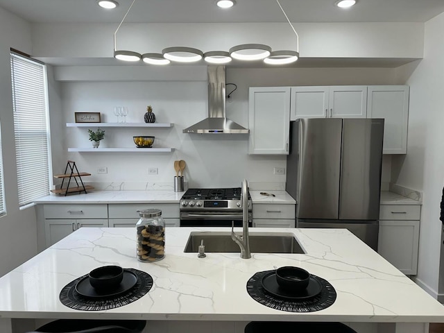 kitchen featuring wall chimney range hood, light stone countertops, a center island with sink, stainless steel appliances, and sink