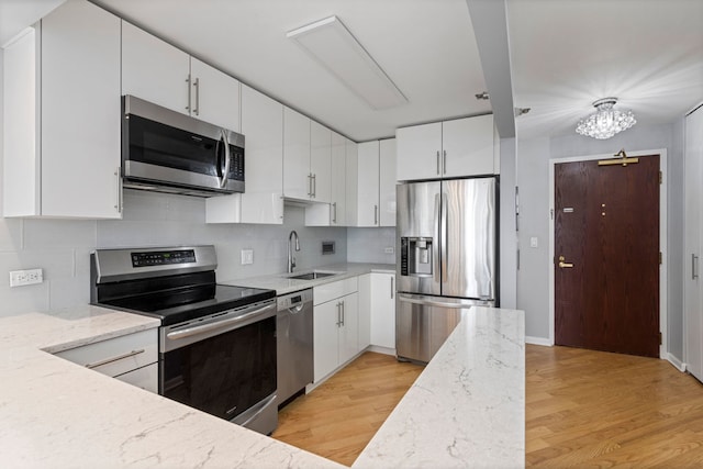 kitchen featuring light hardwood / wood-style floors, white cabinetry, light stone countertops, appliances with stainless steel finishes, and sink