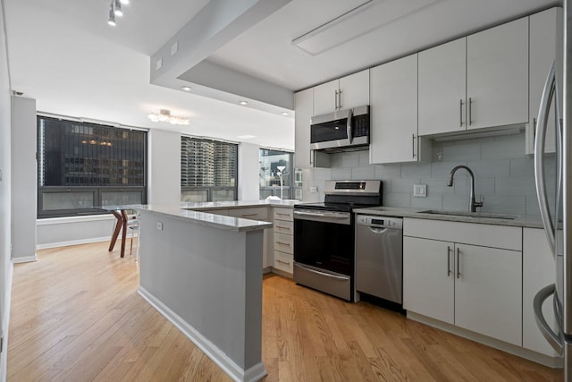 kitchen with stainless steel appliances, kitchen peninsula, light wood-type flooring, and sink