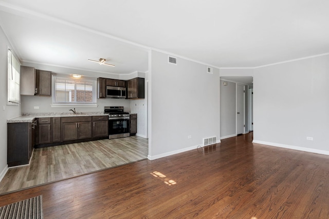 kitchen featuring dark brown cabinetry, hardwood / wood-style floors, ornamental molding, appliances with stainless steel finishes, and sink