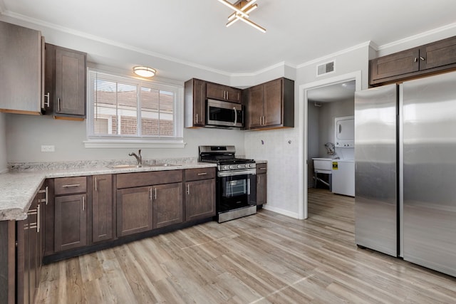 kitchen with dark brown cabinets, light hardwood / wood-style floors, stainless steel appliances, stacked washer and clothes dryer, and sink