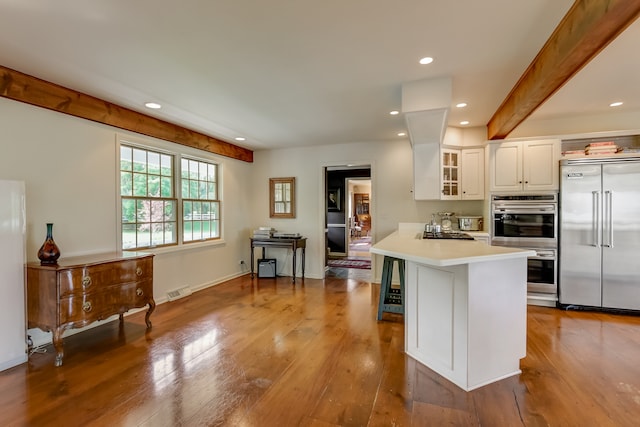 kitchen with light wood-type flooring, beamed ceiling, white cabinets, kitchen peninsula, and appliances with stainless steel finishes