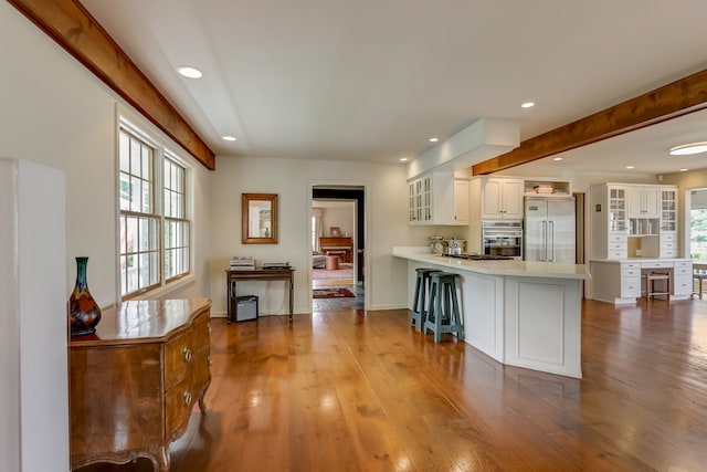 kitchen featuring white cabinets, kitchen peninsula, stainless steel appliances, a breakfast bar area, and light wood-type flooring