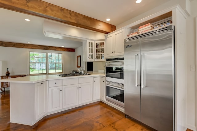 kitchen with beam ceiling, kitchen peninsula, white cabinetry, appliances with stainless steel finishes, and dark hardwood / wood-style floors