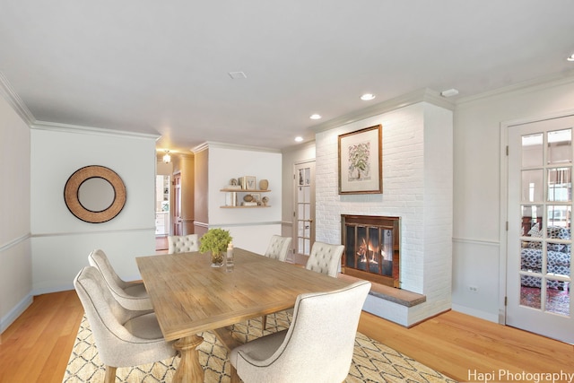 dining space with light wood-type flooring, a healthy amount of sunlight, a fireplace, and ornamental molding