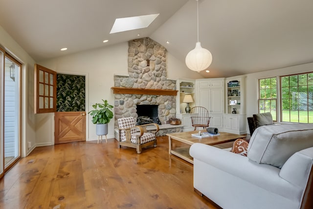 living room featuring vaulted ceiling with skylight, light hardwood / wood-style floors, and a stone fireplace