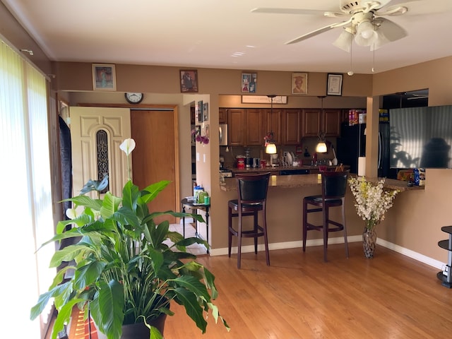 kitchen featuring kitchen peninsula, ceiling fan, light wood-type flooring, black refrigerator, and a breakfast bar