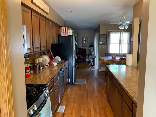 kitchen with appliances with stainless steel finishes, light stone countertops, hardwood / wood-style flooring, and ceiling fan