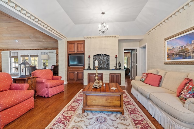 living area featuring brick wall, a notable chandelier, a tray ceiling, and wood finished floors