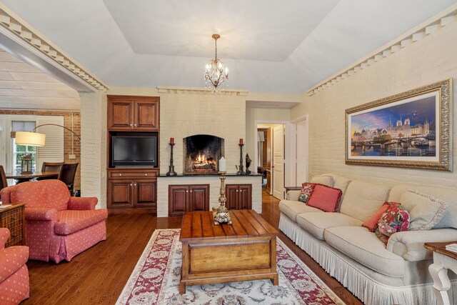 living room featuring dark wood-type flooring, a chandelier, a tray ceiling, and a fireplace