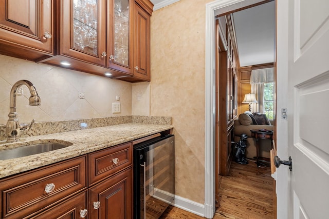 kitchen with light stone counters, beverage cooler, a sink, light wood-type flooring, and decorative backsplash