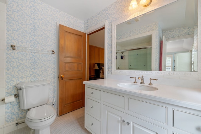 bathroom with toilet, vanity, a shower with shower door, and wallpapered walls