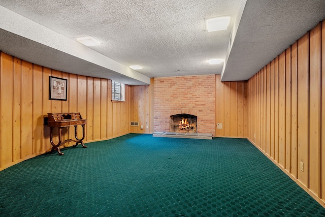 below grade area with a textured ceiling, wood walls, a fireplace, visible vents, and carpet