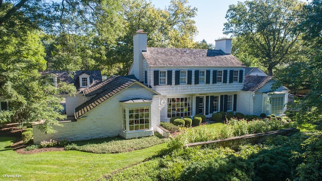 back of house featuring a chimney and a lawn