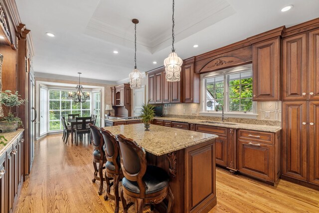 kitchen with a center island, light hardwood / wood-style floors, a tray ceiling, decorative light fixtures, and backsplash