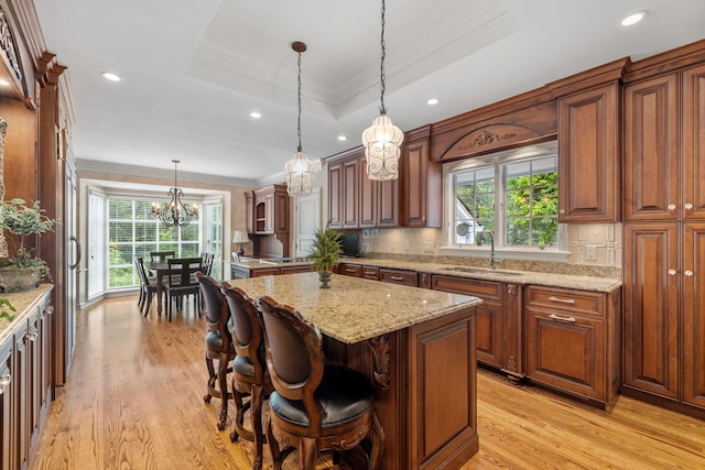 kitchen with decorative backsplash, ornamental molding, a center island, a tray ceiling, and a sink