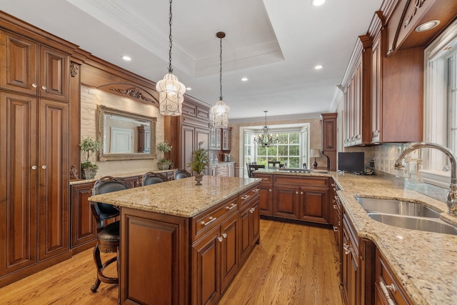 kitchen with light hardwood / wood-style flooring, pendant lighting, a raised ceiling, a kitchen island, and sink