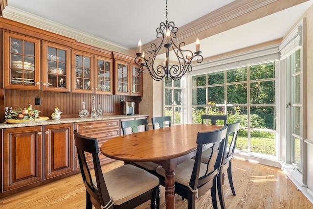 dining area with crown molding, light wood-type flooring, and an inviting chandelier