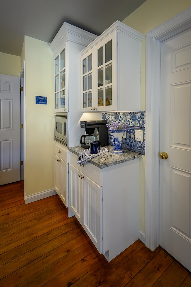 kitchen featuring dark hardwood / wood-style flooring, tasteful backsplash, light stone counters, white cabinetry, and stainless steel microwave