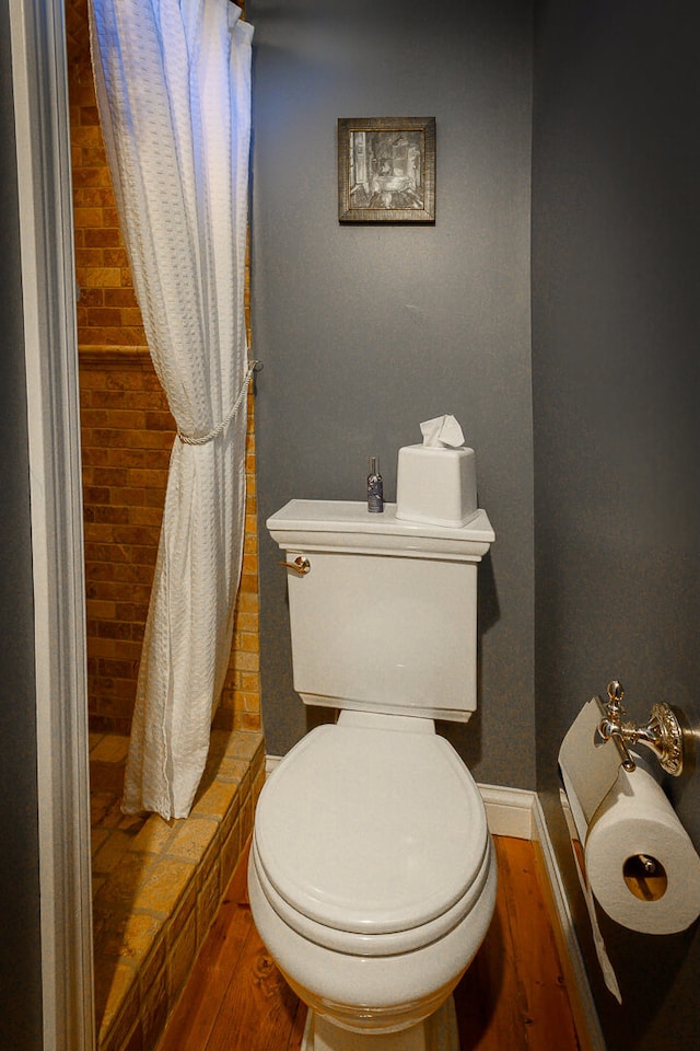 bathroom with hardwood / wood-style floors, toilet, and brick wall
