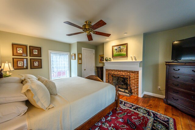bedroom featuring ceiling fan, dark hardwood / wood-style floors, and a brick fireplace