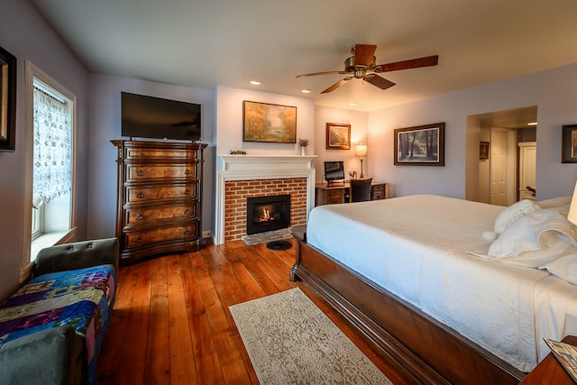 bedroom with multiple windows, dark hardwood / wood-style floors, a brick fireplace, and ceiling fan