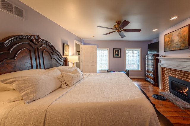 bedroom featuring ceiling fan, wood-type flooring, and a brick fireplace