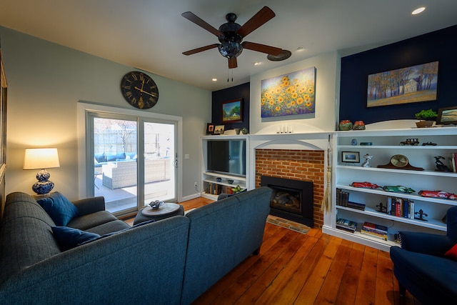 living room featuring ceiling fan, dark hardwood / wood-style flooring, and a brick fireplace