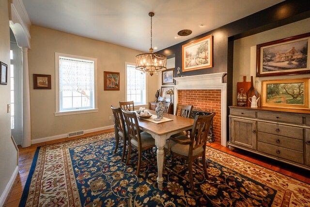 dining space featuring hardwood / wood-style floors, a chandelier, and a brick fireplace