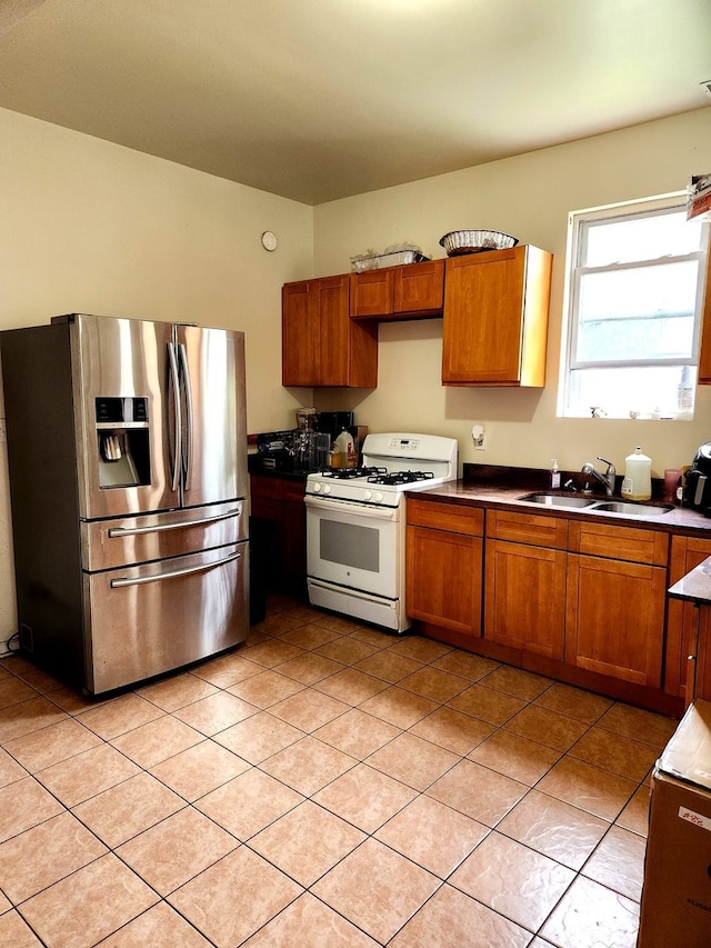 kitchen with light tile patterned flooring, stainless steel refrigerator with ice dispenser, white gas range, and sink