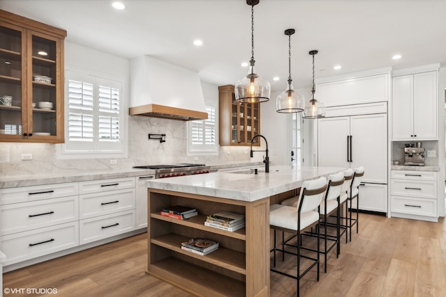 kitchen with a center island with sink, custom range hood, light hardwood / wood-style flooring, white cabinets, and tasteful backsplash