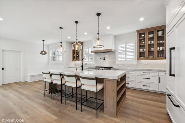 kitchen with light hardwood / wood-style floors, a center island with sink, white cabinets, a breakfast bar area, and tasteful backsplash