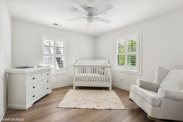 bedroom featuring a crib, ceiling fan, and hardwood / wood-style flooring