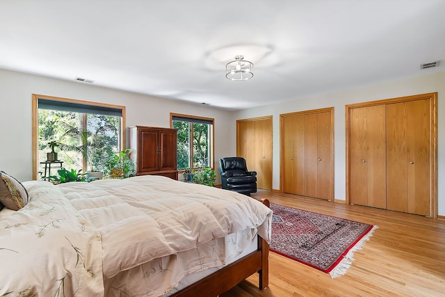 bedroom featuring light wood finished floors, visible vents, and multiple closets