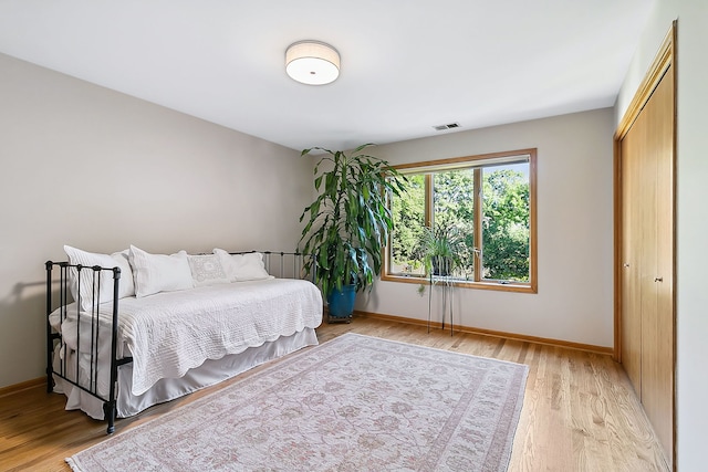 bedroom with light wood finished floors, visible vents, baseboards, and a closet