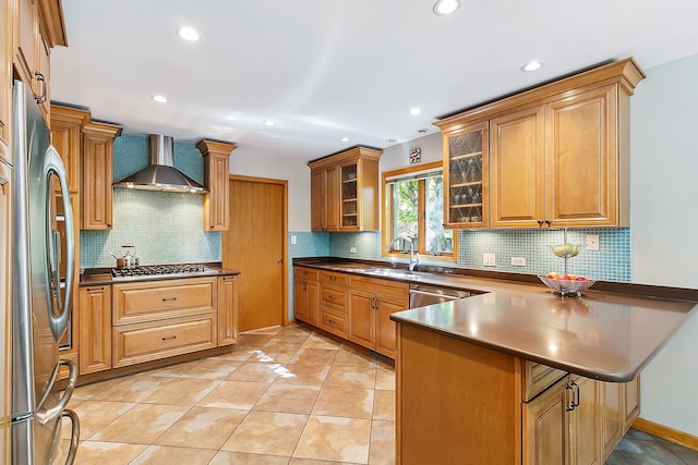 kitchen featuring glass insert cabinets, a sink, stainless steel appliances, a peninsula, and wall chimney range hood