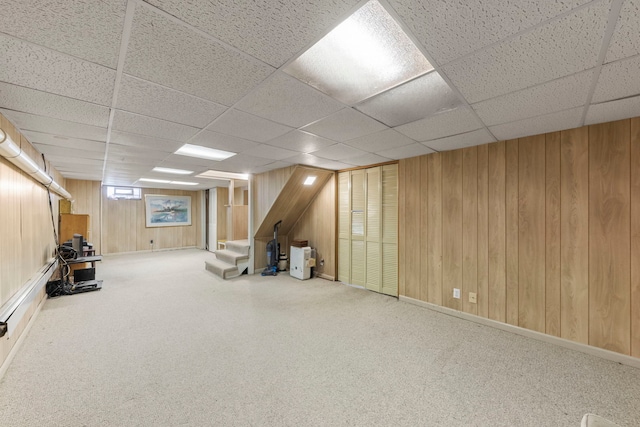 basement featuring carpet floors, a paneled ceiling, and wood walls