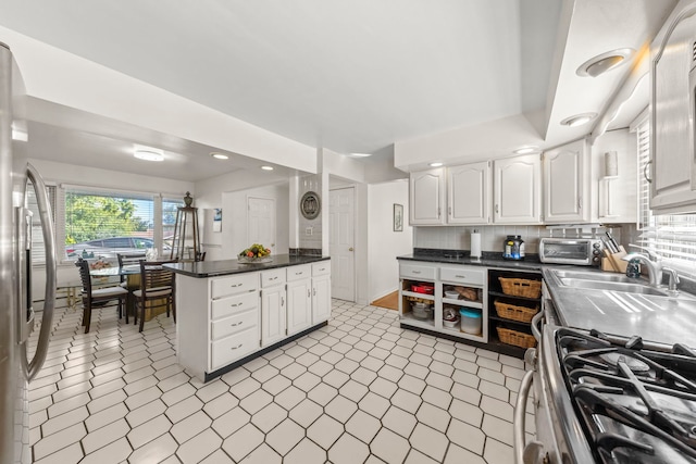 kitchen featuring sink, appliances with stainless steel finishes, tasteful backsplash, white cabinets, and kitchen peninsula