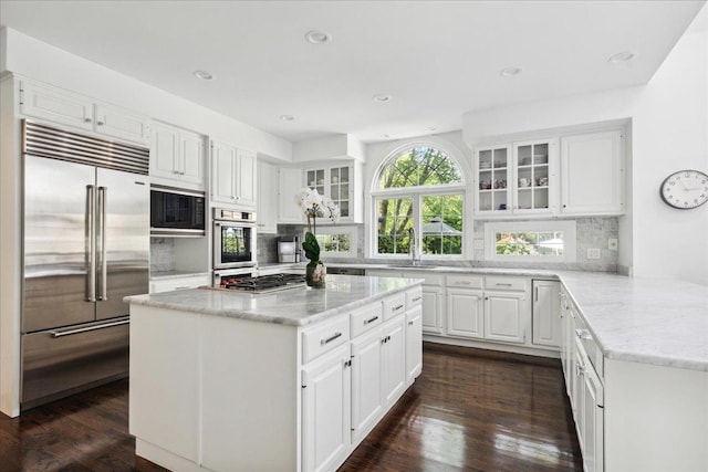 kitchen featuring white cabinetry, light stone counters, built in appliances, dark hardwood / wood-style flooring, and backsplash