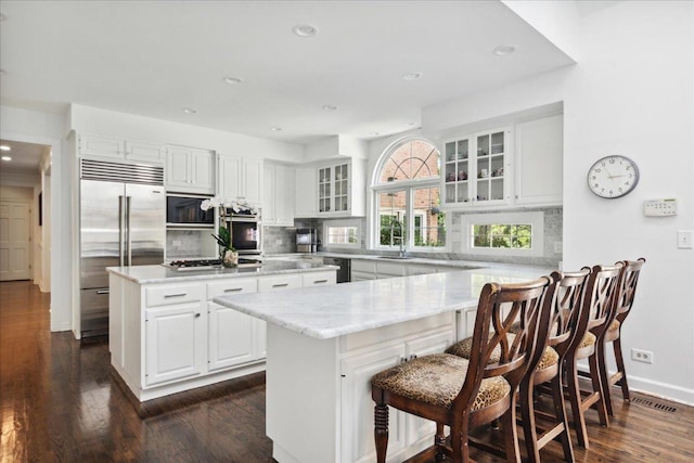 kitchen with sink, a kitchen breakfast bar, built in appliances, white cabinets, and a kitchen island