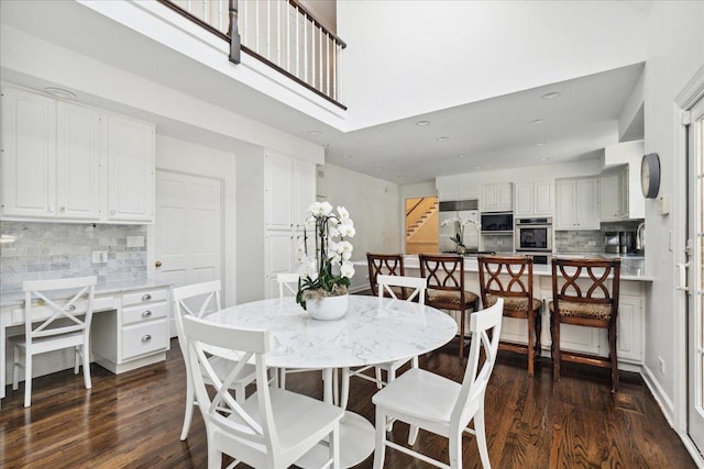 dining space featuring dark wood-type flooring, built in desk, and a towering ceiling