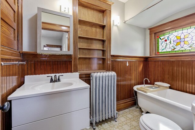 bathroom featuring radiator, wooden walls, vanity, toilet, and a bath