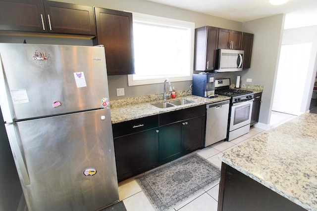 kitchen featuring light stone countertops, sink, dark brown cabinets, light tile patterned floors, and appliances with stainless steel finishes