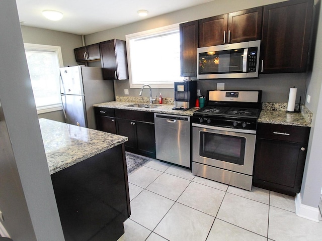 kitchen featuring light stone countertops, dark brown cabinetry, stainless steel appliances, sink, and light tile patterned floors