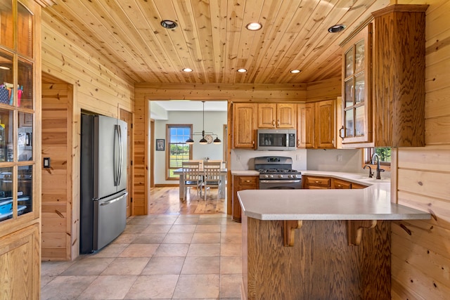 kitchen featuring appliances with stainless steel finishes, light wood-type flooring, pendant lighting, wooden walls, and wooden ceiling