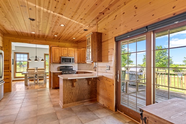 kitchen with light tile flooring, hanging light fixtures, stainless steel appliances, wood walls, and wood ceiling