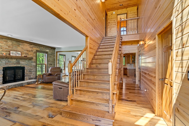 staircase featuring a stone fireplace, wood ceiling, wooden walls, and light hardwood / wood-style flooring